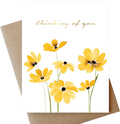 A white greeting card with yellow watercolor flowers and the words 'thinking of you' in gold script, shown with a brown kraft envelope behind it on a white background.