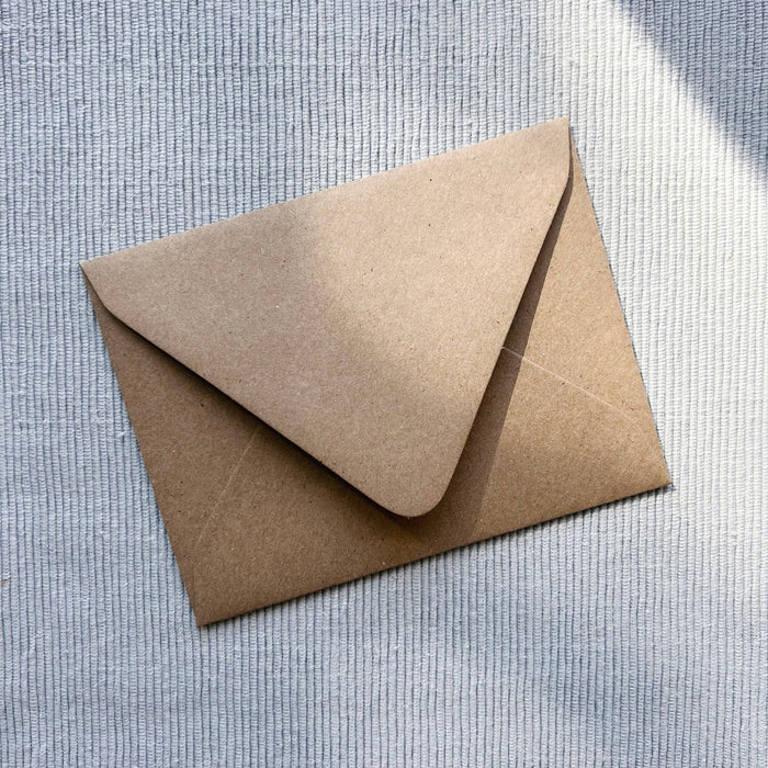 Kraft paper greeting card envelope closed on textured white background
