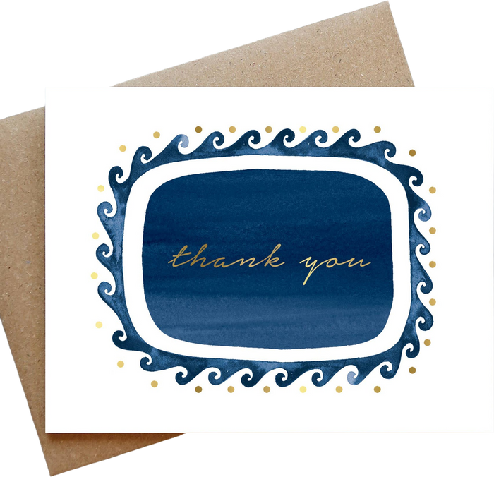 A square white greeting card with a decorative navy blue and gold border and the words 'thank you' in gold script, shown with a brown kraft envelope behind it on a white background.
