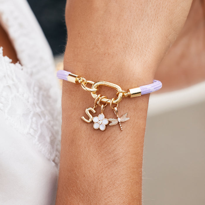 Bracelet with gold chain and charms on a wrist against a neutral background