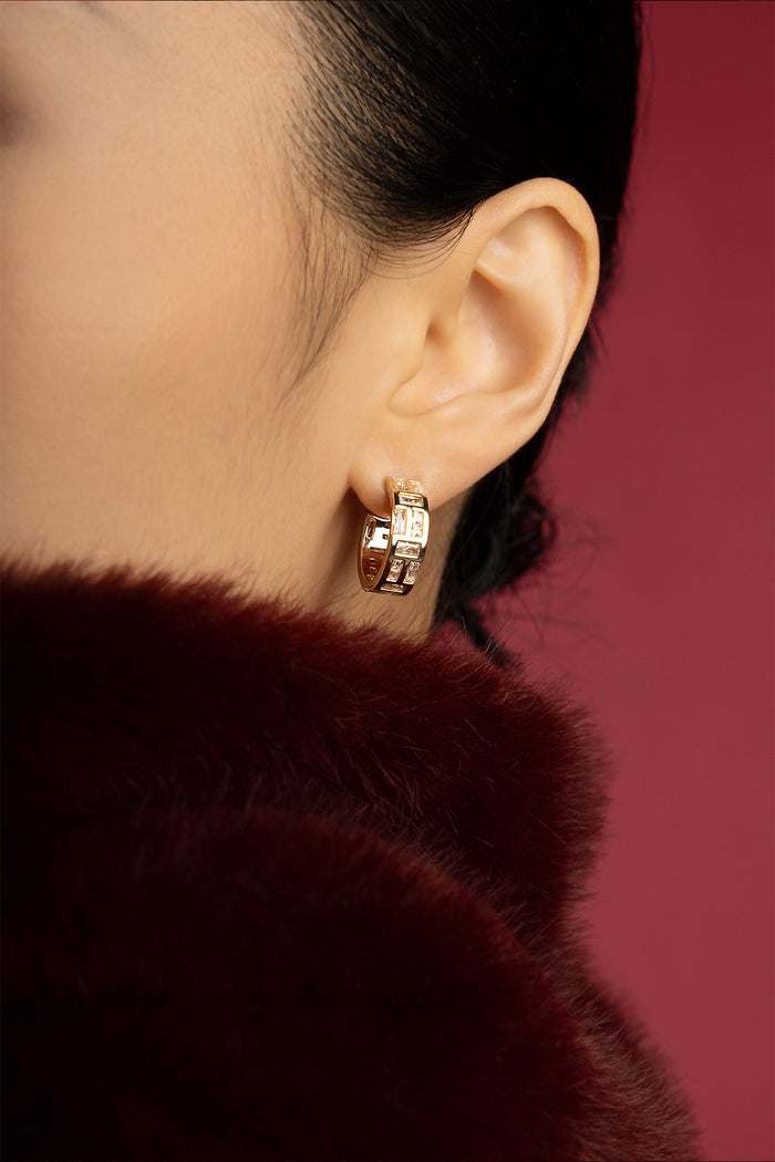 Woman wearing APM Monaco hoop earrings, a golden whisper against winter's warmth.