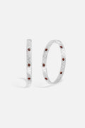 APM Hoop Earrings, brushed rhodium finish glowing with deep red accents.