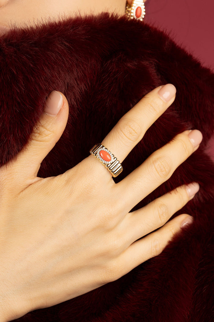 Woman wearing APM Monaco ring, coral warmth against burgundy fur, quiet winter elegance.