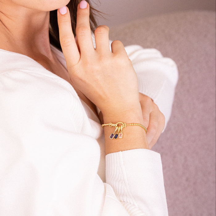 Woman wearing a gold bracelet on her wrist, with a neutral background