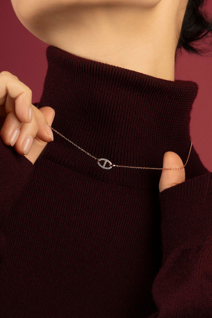 Woman wearing APM Monaco necklace, a delicate rose glow against burgundy warmth.