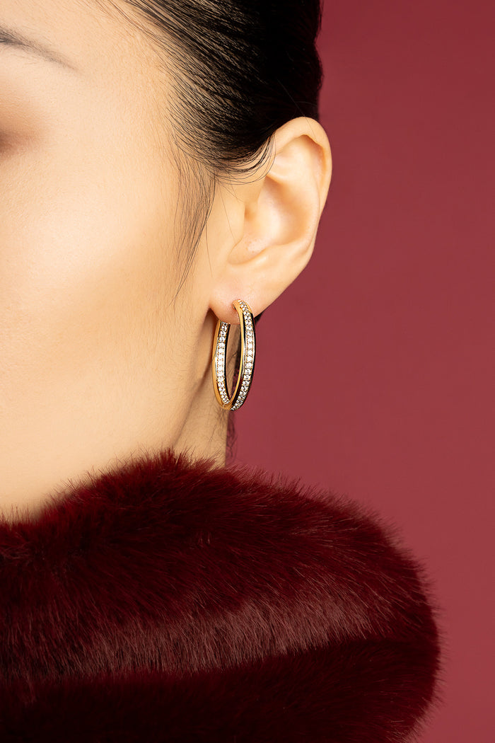 Woman wearing APM hoop earrings, a golden shimmer against deep burgundy elegance.