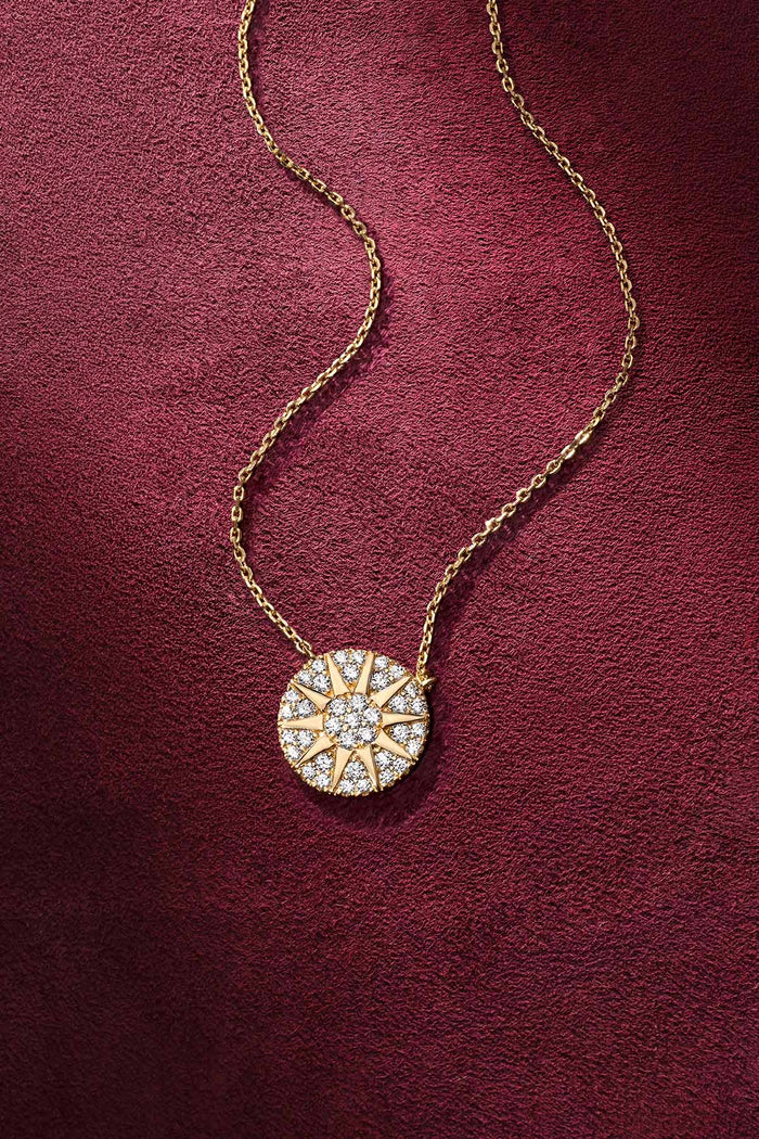 APM Necklace glowing in gold, a radiant sun on velvet burgundy.