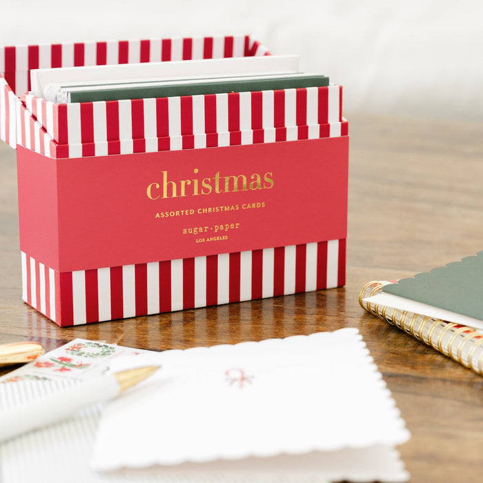 Red and white striped Christmas card box by Sugar Paper displayed on wooden desk with stationery.