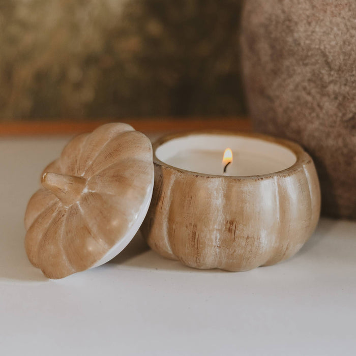 Pumpkin-shaped soy candle in wooden jar with lid, lit flame, autumn home decor