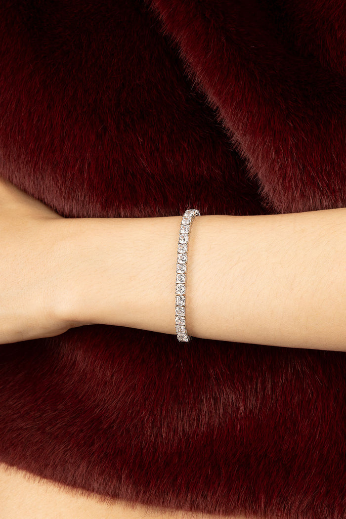 Woman wearing APM Monaco tennis bracelet, quiet sparkle against deep burgundy elegance.