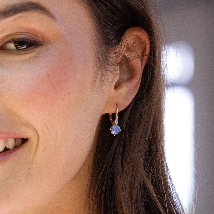Close-up of a woman wearing a gold earring with a blue gemstone.